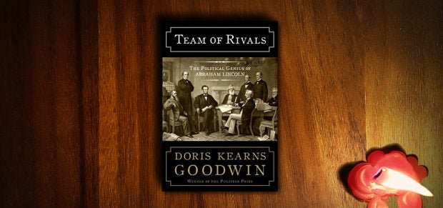 Buch mit schwarz-Braunem Einband liegt auf einer braunen Tischplatte, daneben eine heruntergebrannte rote Kerze