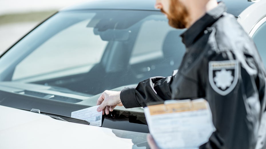 Ein Polizeibeamter steht an einem geparkten Auto. (Symbolfoto: Ross Helen/Shutterstock) Berliner Polizei warnt: Abzocke mit QR-Codes auf gefälschten Strafzetteln