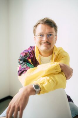 Jannis Johannmeier lehnt sich in einer bunten Jacke über einen Stuhl.