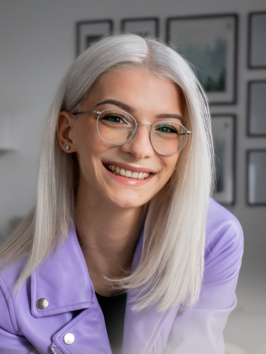 Sabina Pawlowska sitzt in einer fliederfarbenen Jacke vor einer hellen Wand.