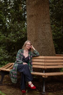 Dorthe Hodemacher sitzt auf einer Bank, die sich um einen Baum zieht. 