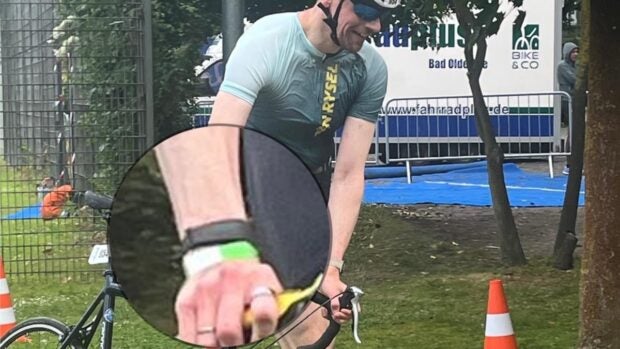 Ein Mann im Sportoutfit schiebt ein Rennrad. Das Handgelenk wurde vergrößert, um das Fitbit Air zu zeigen.