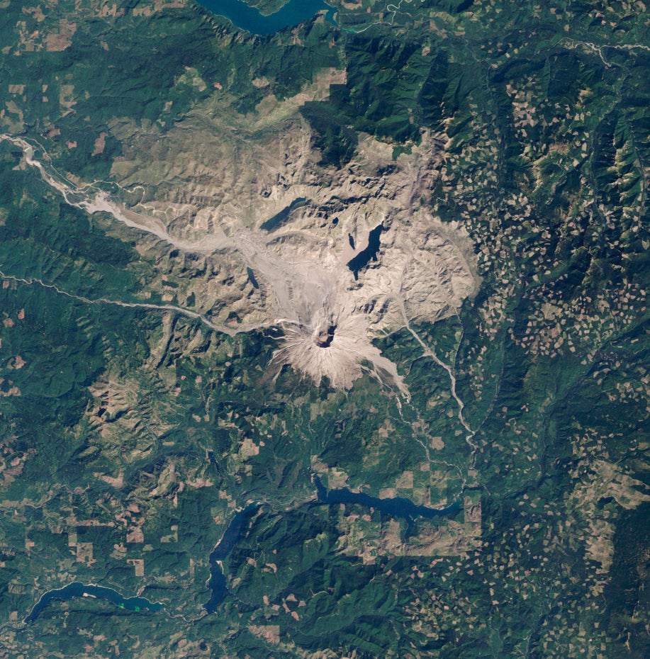 Mittig im Bild ist der Mount St. Helens und die ihn umgebende grau-braune Vulkanlandschaft zu sehen.