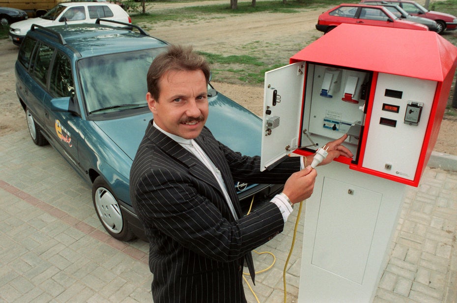 Ein Mann im Nadelstreifen steckt ein Elektroauto an einer Ladesäule an