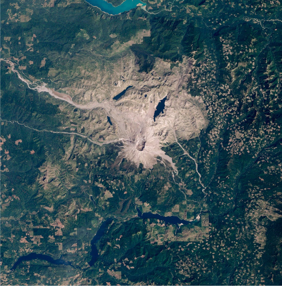 Grüne Landschaft wird oben und unten im Bild von Stauseen durchzogen, mittig liegt die grau-braune Vulkanlandschaft des Mount St. Helens.