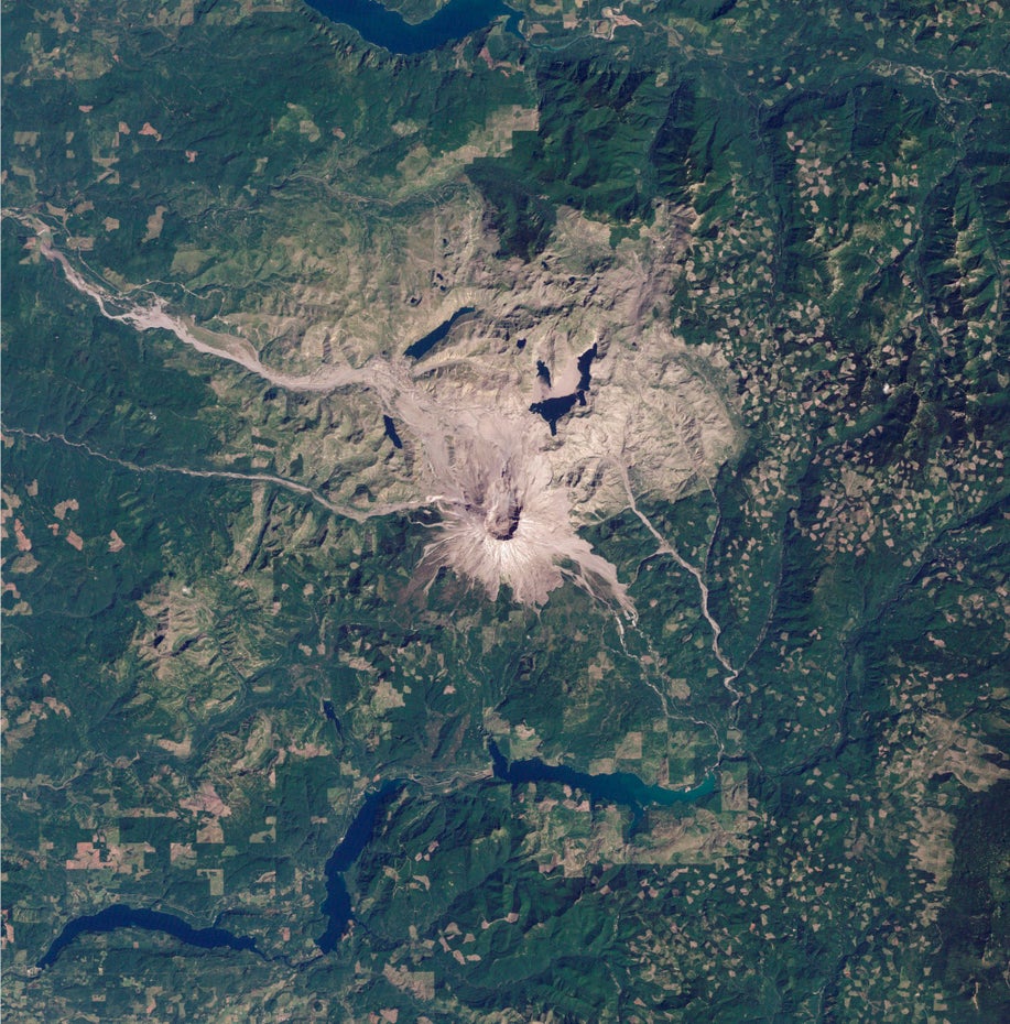 Grüne Landschaft dominiert die Satelliten-Aufnahme, mittig im Bild ist in grau-braun der Vulkan Mount St. Helens und die ihn umgebende Vulkanlandschaft zu sehen.