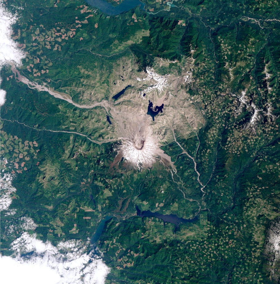 Grüne Landschaft umgibt den grau-braunen Mount St. Helens und seine Vulkanlandschaft, oben und unten im Bild sind blaue Stauseen zu sehen.