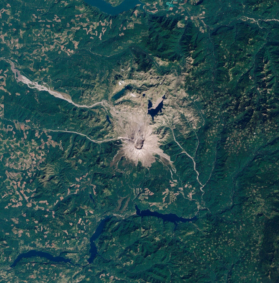 Die Satelliten-Aufnahme zeigt eine grüne Landschaft, in deren Mitte in grau-braun der Vulkan Mount St. Helens und seine Vulkanlandschaft liegen.