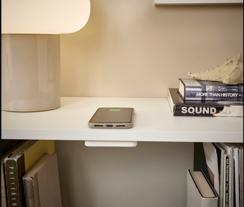 Ein Smartphone liegt auf einem Regalbrett, unter dem ein Ladepad von Ikea befestigt ist