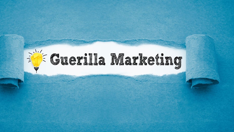 In schwarzer Schrift steht auf weißem Untergrund „Guerilla Marketing”, links daneben ist eine Glühbirne gemalt.