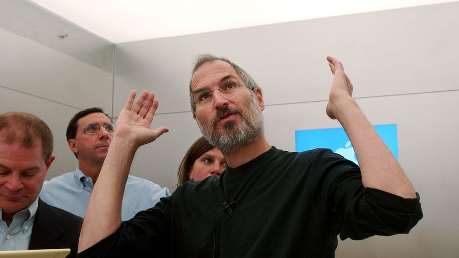 Steve Jobs gestikuliert und erklärt umstehenden Männern etwas. 