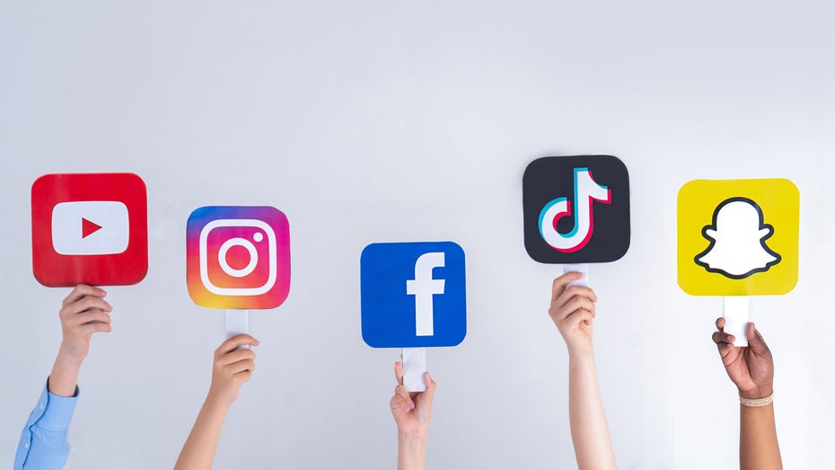 Das jeweilige Logo von Youtube, Instagram, Facebook, Tiktok und Snapchat ist zu sehen; Hände halten sie hoch.