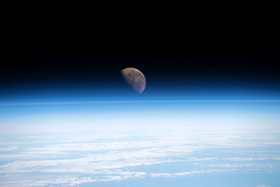 Der Mond ist hinter den bläulich leuchtenden atmosphärischen Schichten der Erde zu erkennen.