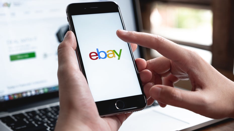 Eine Person hält ein Smartphone mit Ebay-Logo in der Han