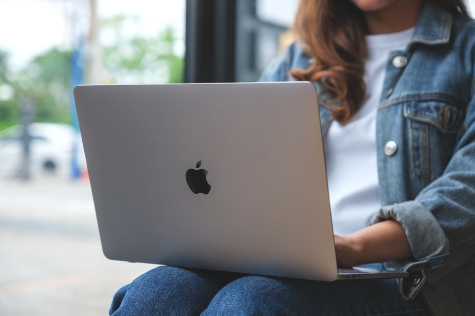 Eine Frau hat ein aufgeklapptes Mac-Book auf den Oberschenkeln liegen.