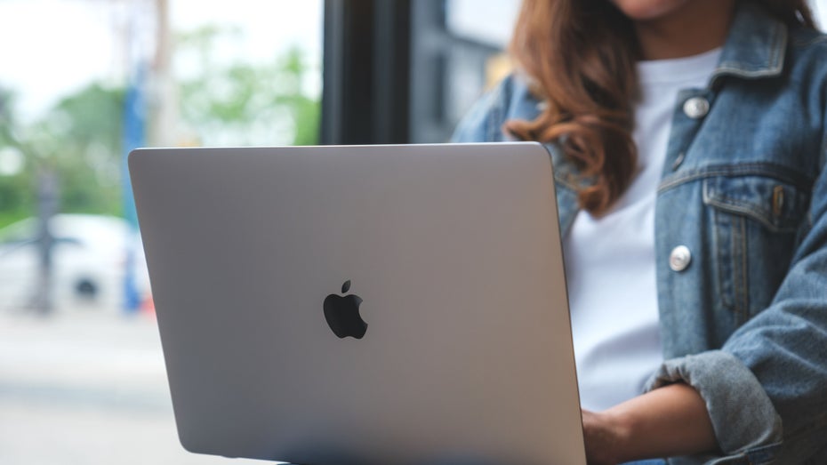 Eine Frau hat ein aufgeschlagenes MacBook auf ihren Oberschenkeln liegen.